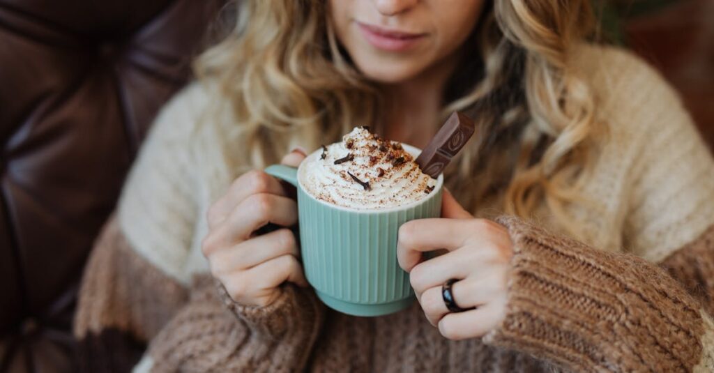 A woman enjoys hot cocoa with whipped cream in a cozy setting, perfect for autumn.