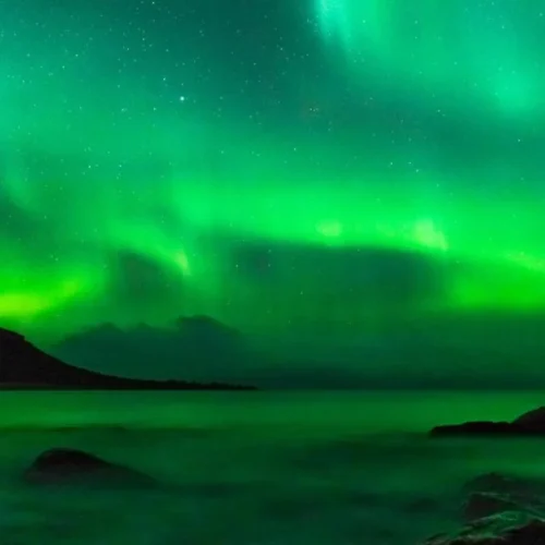 Vibrant green aurora borealis over tranquil sea.